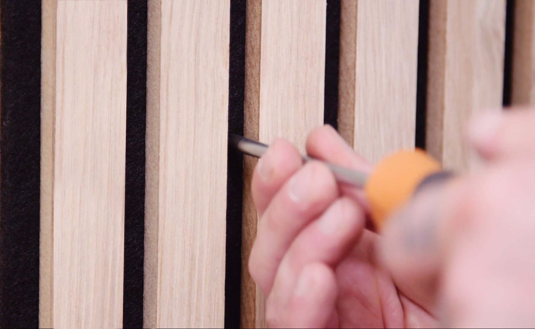 Close-up of a person using an orange-handled screwdriver to adjust wooden slats in a furniture piece, highlighting the texture and natural grain of the wood. 