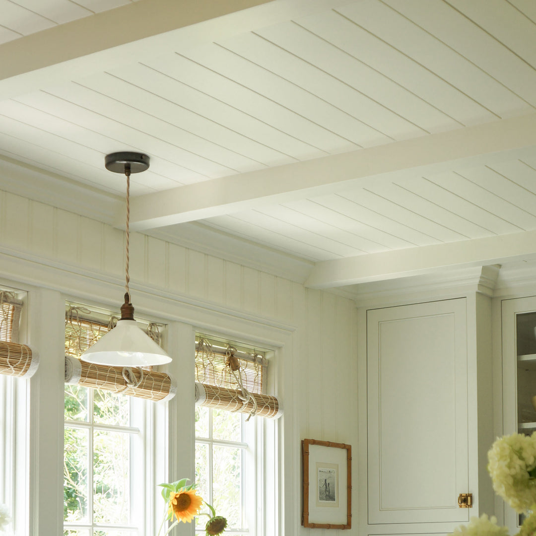 A white shiplap ceiling with exposed beams in a bright, modern kitchen setting, featuring a hanging pendant light, windows with woven shades, and white cabinetry.