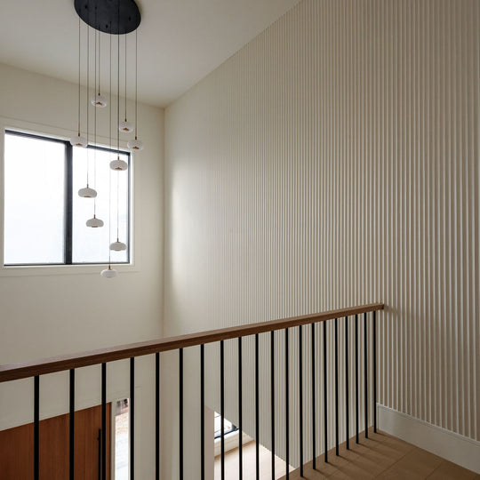 Modern interior entryway with fluted white wall paneling, wooden handrail, black metal balustrade, and a multi-light pendant chandelier.