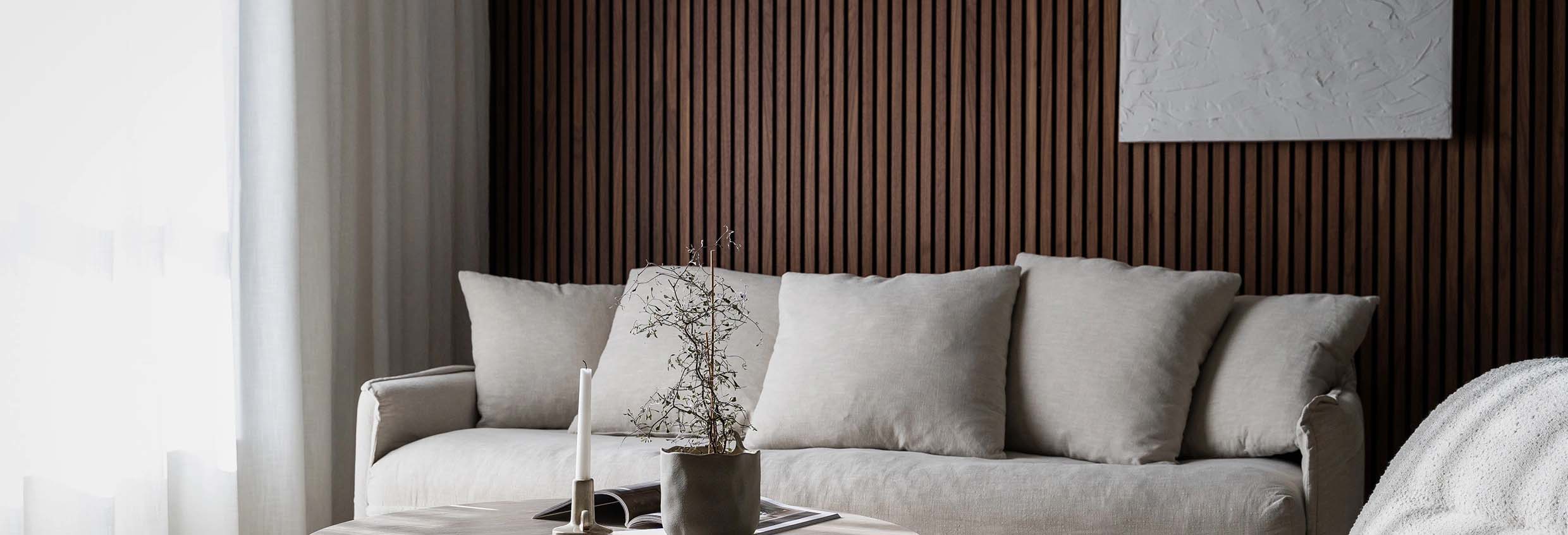 A nordic living room with minimalist decor, featuring a grey sofa against a backdrop of elegant wood slat wall panels and a white abstract art piece.