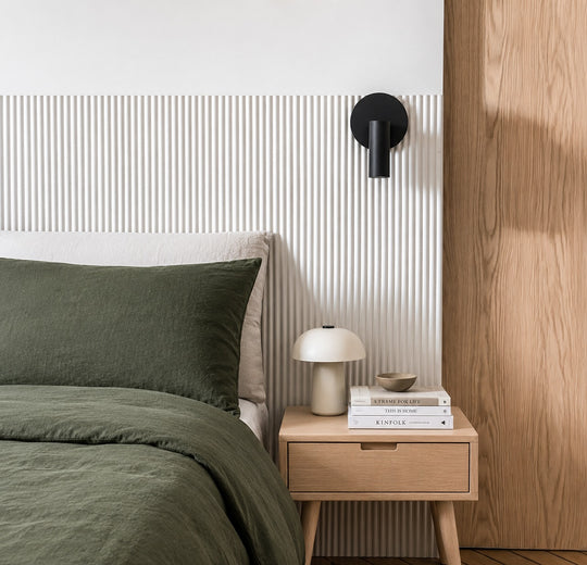 A styled bedroom corner featuring a bed with dark olive green bedding and a tambour wall paneling behind the headboard.