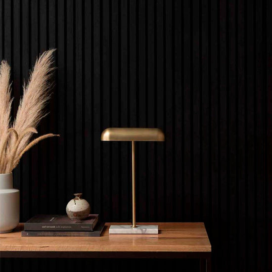 modern gold lamp on wooden desk next to vase with pampas against a black slat wood wall